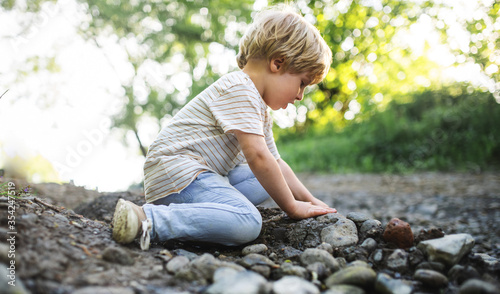 Side view of small boy playing with rocks and mud in nature.