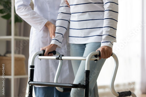 Cropped image caregiver helping to disabled patient walking with rollator equipment reduce load and joint pain with arthritis. Physical therapist and therapy, neurological cerebellar disorders concept