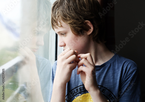 Cute 12 years old autistic boy looking through the window