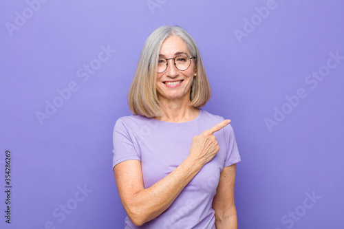 senior or middle age pretty woman smiling cheerfully, feeling happy and pointing to the side and upwards, showing object in copy space