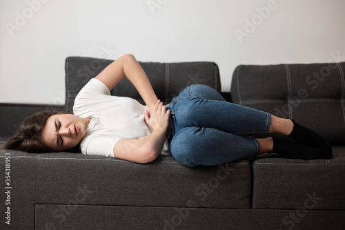 young beautiful brunette woman lying on the sofa suffering from extreme pain in stomach during periods looking desperate, healthcare and medical concept