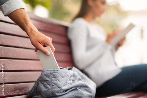 Pickpocket Thief Stealing Mobile Phone From Woman's Bag In Park