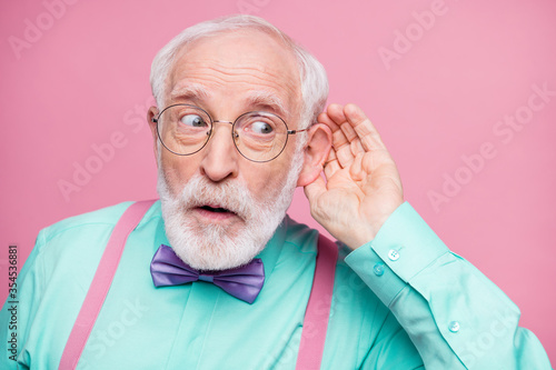 Closeup photo of attractive grandpa hand near ear listen rumors focused chatterbox bad person wear specs mint shirt suspenders violet bow tie isolated pink pastel color background