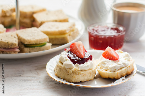 Traditional English afternoon tea: scones with clotted cream and jam, strawberries, with various sadwiches on the background, selective focus
