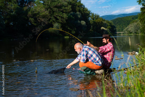 Angler catching the fish. Senior man fishing. Bearded brutal hipsters fishing. Men relaxing nature background. Against the background of the water with a reflection of the forest. Fishing.