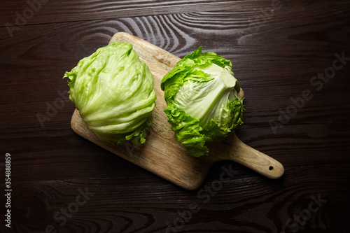 Iceberg lettuce on cutting board on wooden table background. Whole heads of fresh crisphead lettuce