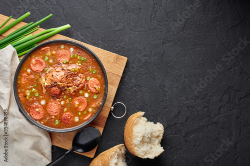 Chicken and Sausage Gumbo soup in black bowl on dark slate backdrop. Gumbo is louisiana cajun cuisine soup with roux. American USA Food. Traditional ethnic meal. Copy space