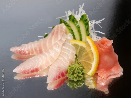 Sea bass sashimi with ginger, wasabi, cucumber and lemon on a shiny surface. Japanese kitchen