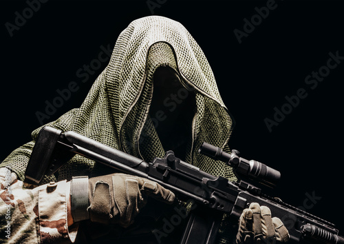 Fully equipped soldier in tactical net scarf with sniper rifle.