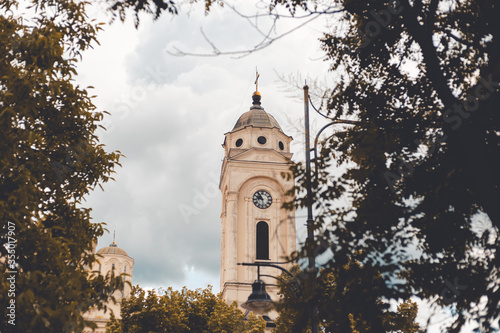 View on church tower through trees, heavy clouds in background.