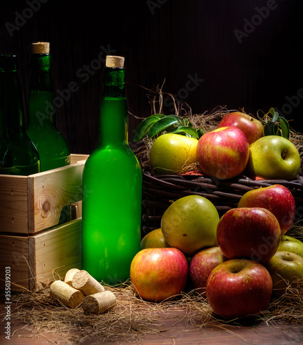 Asturian cider bottles wooden crate with many red and green apples at wicker basket over wooden background