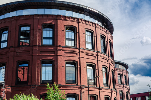 Part of red brick corporate building with sky reflections in the windows against sky with grey clouds background.