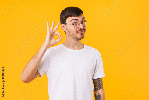 Photo of amusing young man making ok sign and looking at camera