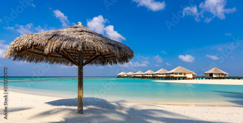 single thatched umbrella on lagoon beach with overwater bungalows in the background