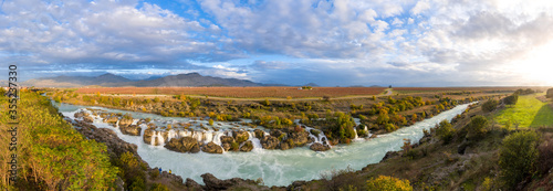 180 degree panorama of a river with rapids and waterfalls under beautiful fluffy clouds in blue sky. Large vineyard in the background. Niagara waterfall on Cijevna (Cem) near Podgorica Montenegro.