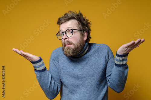 Strange man with an innocent and embarrassed expression on his face shrugs and spreads arms to the sides, on a yellow background.