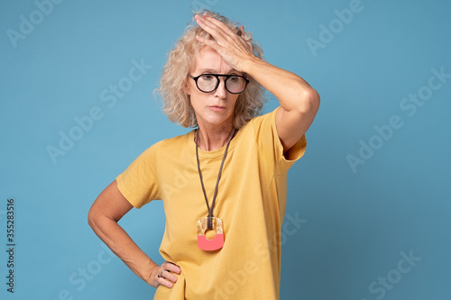 Frustrated forgetful senior woman is worried, puzzled expression on her face, holding hand on head. Grandmother realizes that she forgot to do something important.