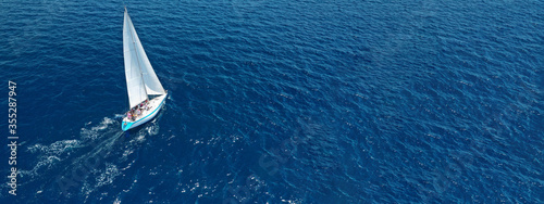 Aerial drone ultra wide photo of beautiful sail boat with white sails sailing open ocean deep blue sea