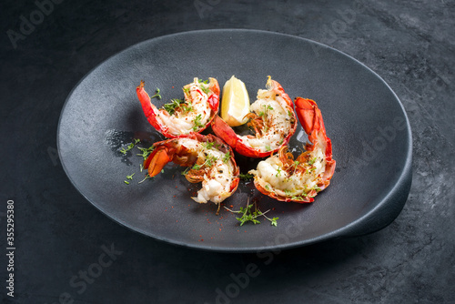 Traditional barbecue spiny lobster tail sliced and offered with lemon slice and herbs as closeup on a modern design plate