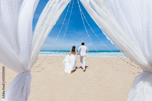 Newlyweds holding hands hugging at white sandy tropical caribbean beach landscape after wedding ceremony of marriage on destination wedding honeymoon travel looking on blue sea in Punta Cana Dominican