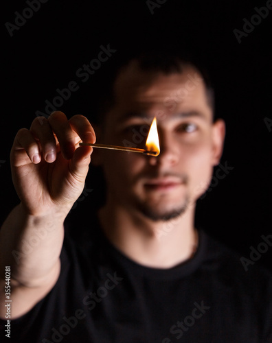 Man holding burning match stick in front of blurred face on dark background