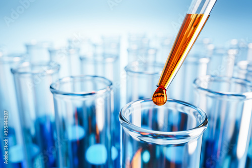 Closeup of test tubes with orange or blue liquid. Dropping glass with an orange drop above. Testing laboratory, SARS-CoV-2 test, chemical testing facility, medical testing. 