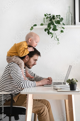 Father working with his baby boy in home office with laptop. Work from home concept