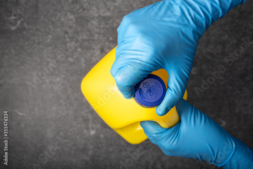 Human hand in protective glove opening a yellow bleach bottle. Disinfection concept