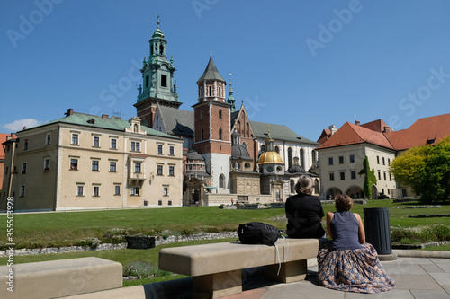 Silhouettes of a tourists sitting on a bench in garden of Wawel Royal Castle in Krakow and looking at the castle. Poland