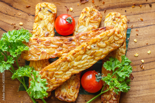 Fried tempeh or tempe (traditional Indonesian soy product), cherry tomatoes and parsley on wooden surface. Top view. 