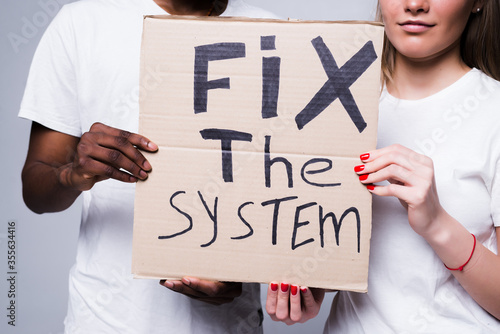 Young african man and coucasian woman holding a cardboard poster with the message text Fix the system isolated on white background. Concept on the theme of protest for police brutality and racism.