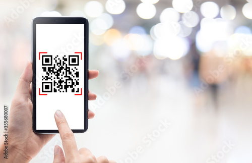 Hand using mobile smart phone scan Qr code on shopping mall background. Barcode reader, Qr code payment, Cashless technology, Digital money concept.