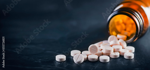 White medical pills or tablets with bottle on black background. Macro side view with copy space