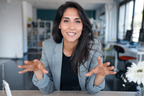 Confident business woman looking and speaking through the webcam while making a video conference from the office.