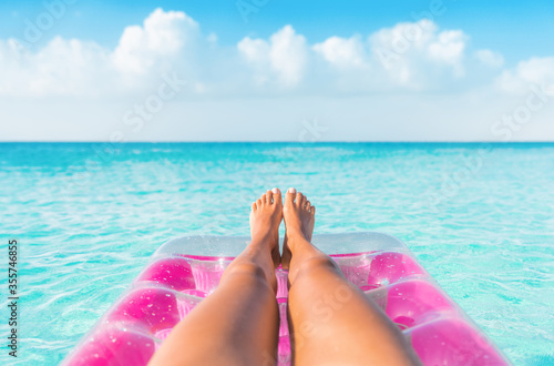 Summer relax vacation woman pov of legs relaxing on pink inflatable pool toy float floating in turquoise water ocean background. Suntan at tropical beach.