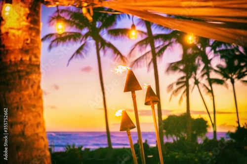 Hawaii luau party with fire torches at sunset. Hawaiian icon, lights burning at dusk at Waikiki beach resort restaurant for outdoor lighting cozy atmosphere.