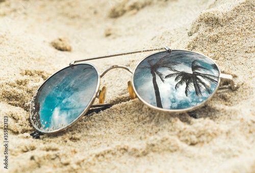 Mirrored sunglasses close up on the beach sand with palm trees reflection