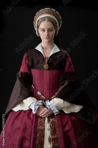 A young woman in a red Tudor dress against a black bacdrop