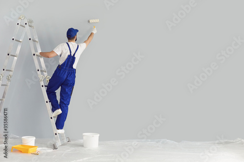 Building contractor painting grey wall with roller brush, copy space text. Construction worker renovating house