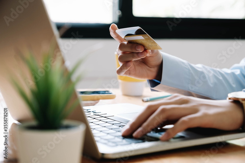 Close up hand of woman holding credit card and using laptop computer at home. Online shopping concept