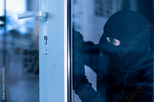 Robber in black balaclava cracking door with metal picklock