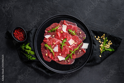 Marbled beef carpaccio with arugula and parmesan cheese. Black background. Top view. Space for text