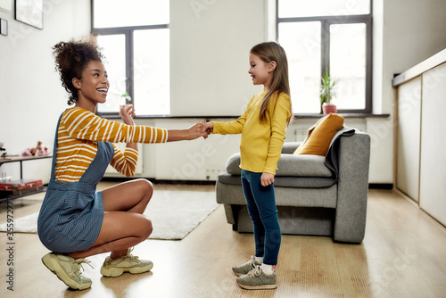 Connected. African american woman baby sitter get acquainted with caucasian cute little girl. They are smiling and talking