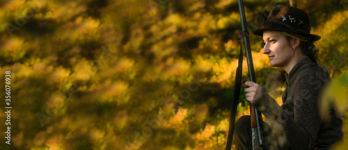 Charm of the setting sun in the mountains. Young beautiful woman on hunting with a gun. Wide banner.