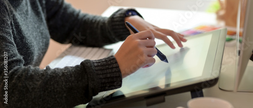 Female graphic designer working on drawing tablet with stylus pen in office room