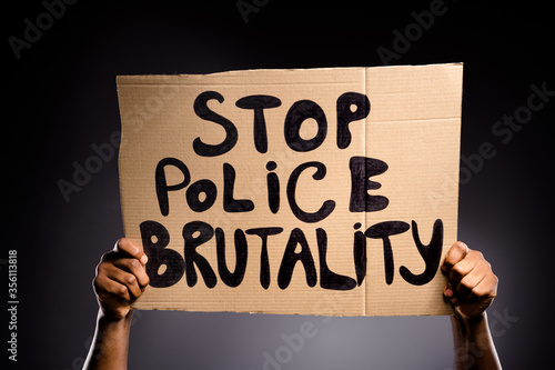 Close up photo of afro american hand hold cardboard banner show stop police brutality message isolated over black color background