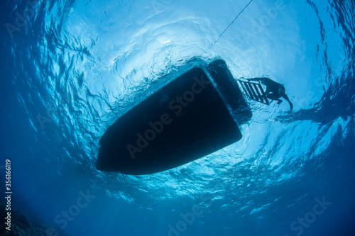 A diver climbs a ladder onto a small boat while floating in the tropical Pacific Ocean near the island of Yap.