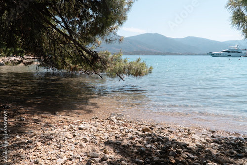 Love Bay on Poros island, Greece. Summer beach with blue sea and white yacht.