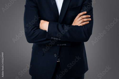business man with crossed arms on grey background isolated while standing serious and firmly in front of camera