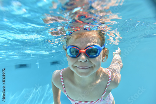 Portrait of cute girl with goggles swimming under pool water